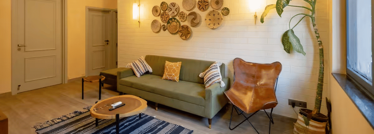 A cosy living room with a cushioned sofa, a small round table on a carpet, warm lighting, and indoor plants at Lime Tree Villa with Private Pool | Luxury Stay in Goa.